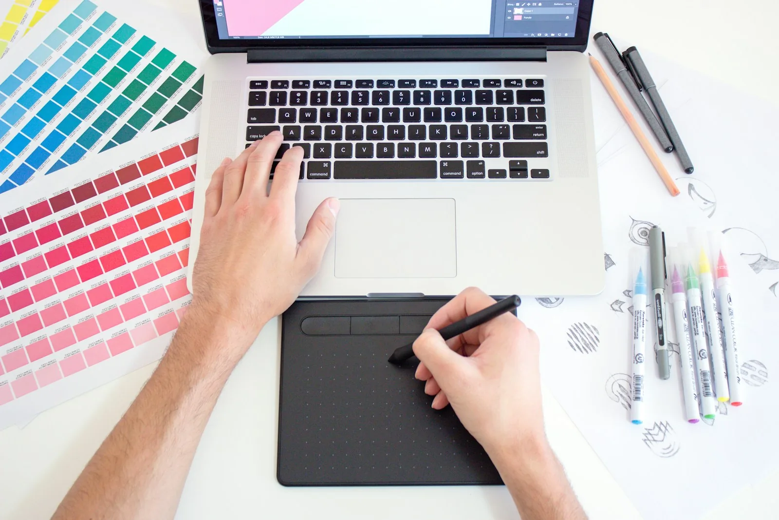 A designer working on a drawing tablet beside colour swatches